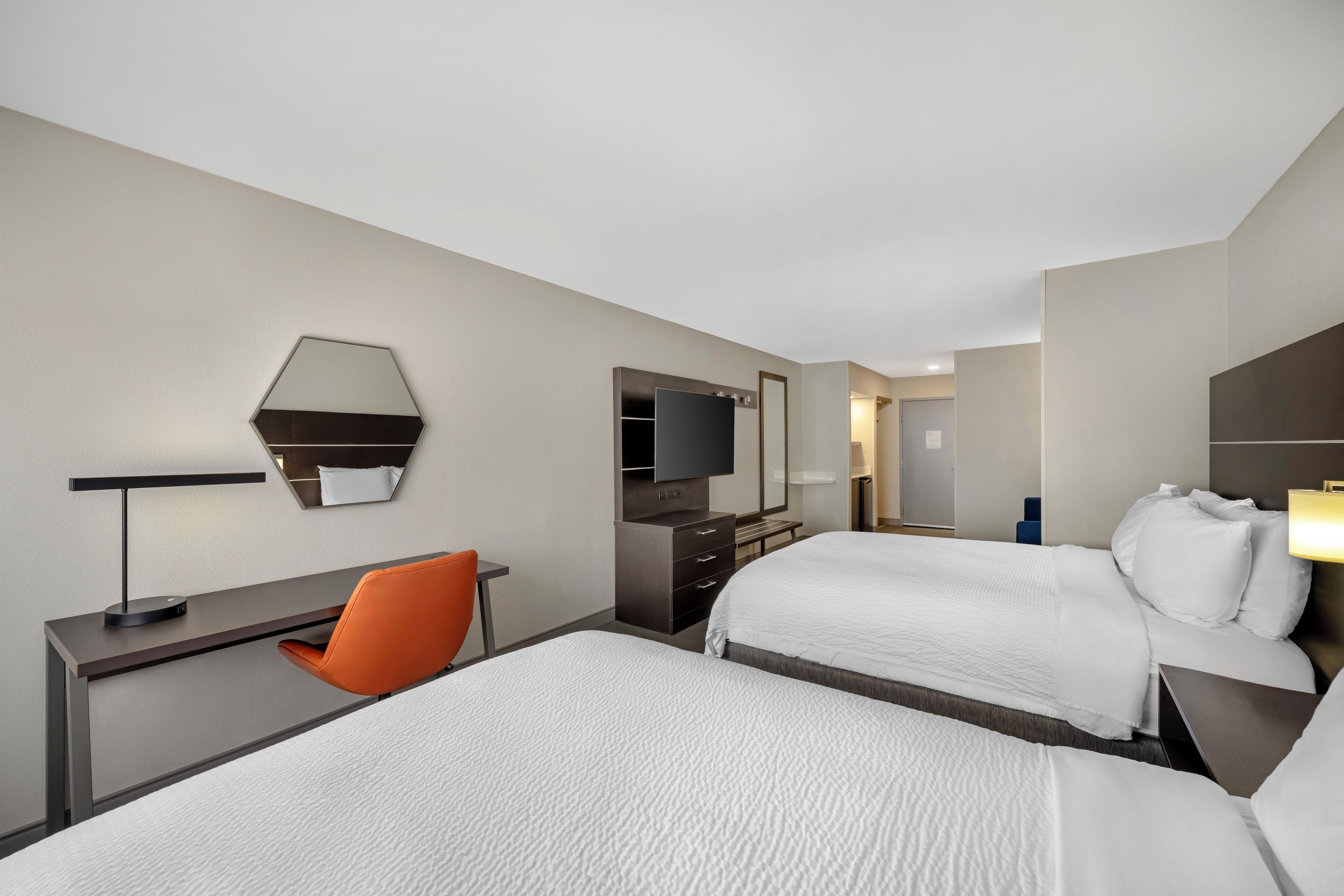 A hotel room with two beds, a desk with a chair, a television, and a mirror.