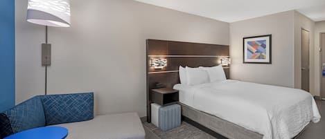 Ein Hotelzimmer mit einem Bett, einem Nachttisch, einer Lampe, einem Sessel und einem kleinen Tisch.
