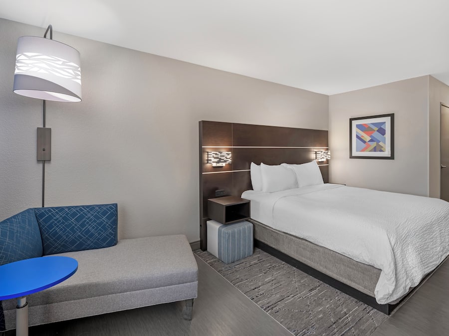 A hotel room with a bed, a bedside table, a lamp, a chair, and a small table.