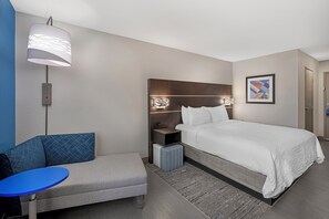A hotel room with a bed, a bedside table, a lamp, a chair, and a small table. - Holiday Inn Express - Balloon Fiesta Park by IHG (Albuquerque)