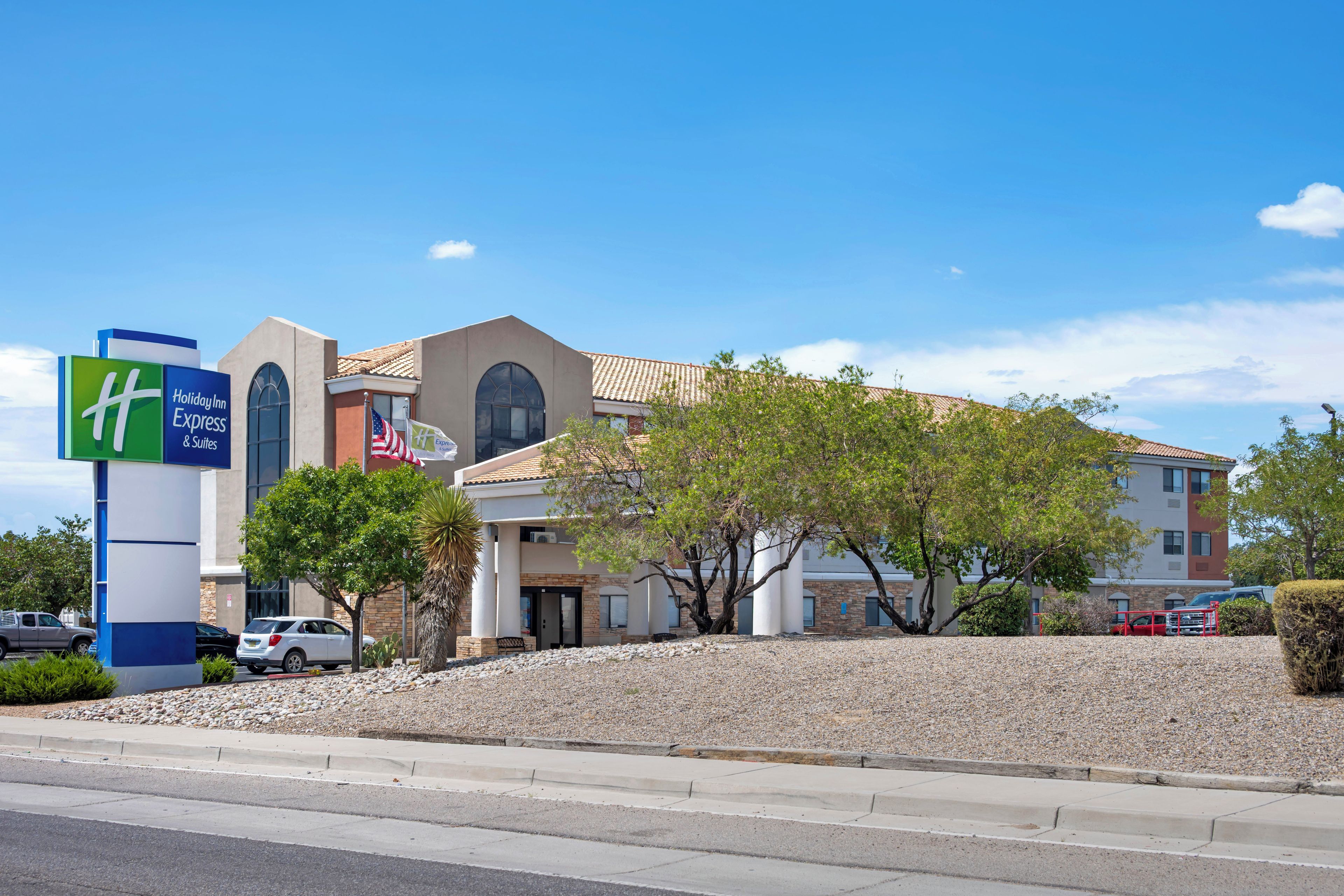 A Holiday Inn Express & Suites hotel with a modern design, featuring a prominent American flag and a clear blue sky.