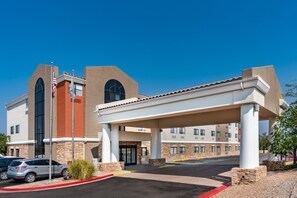 A hotel with a covered parking area, a flag, and a clear blue sky. - Holiday Inn Express - Balloon Fiesta Park by IHG (Albuquerque)