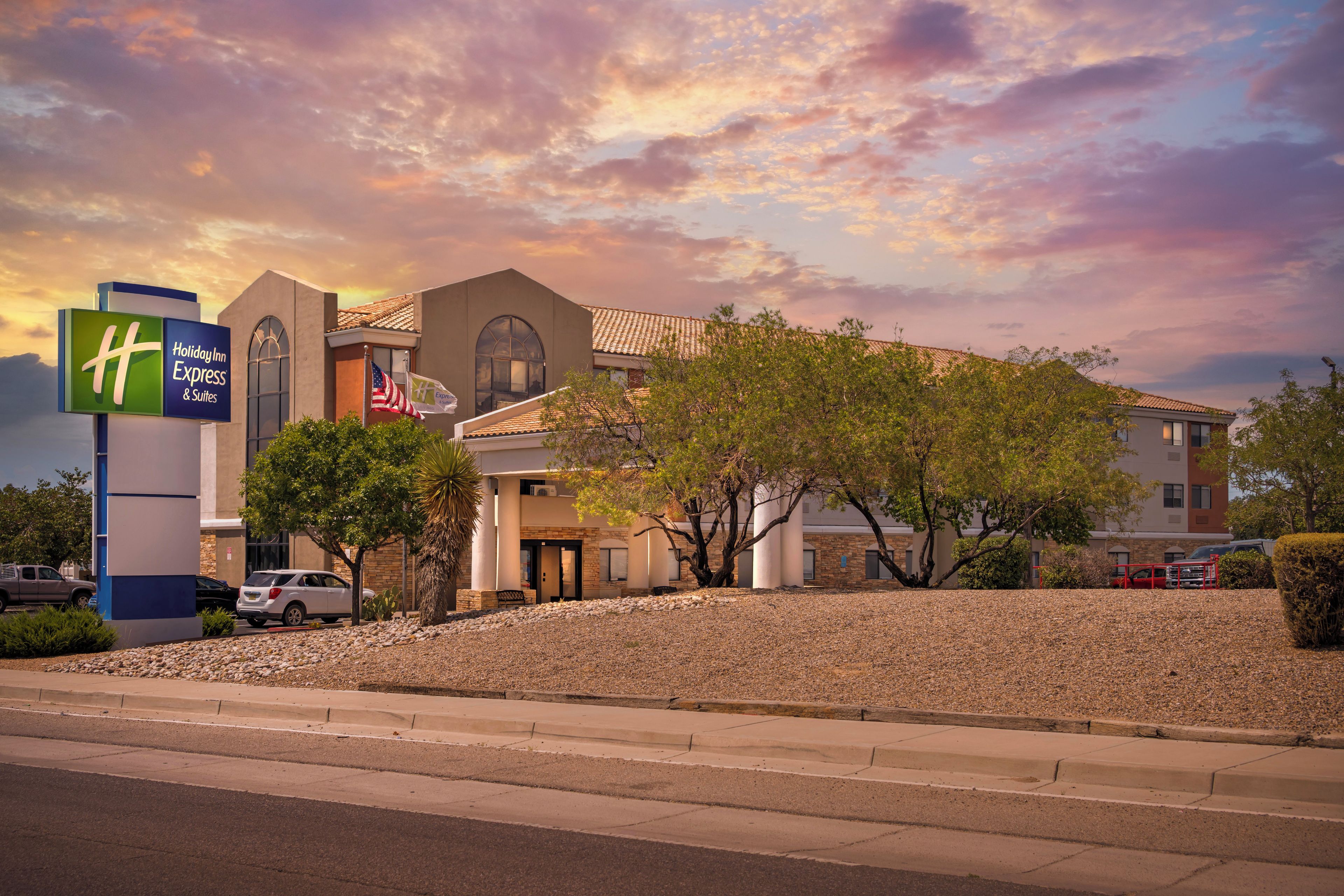 A Holiday Inn Express & Suites hotel with a clear view of the building's architecture, including a prominent entrance and a flagpole with the American flag.
