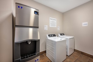 A hotel laundry room with a water fountain, two washing machines, and a sign indicating guest laundry use. - Holiday Inn Express - Balloon Fiesta Park by IHG (Albuquerque)