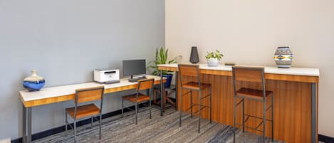 A hotel room with a desk, computer, chairs, a potted plant, and a decorative vase.