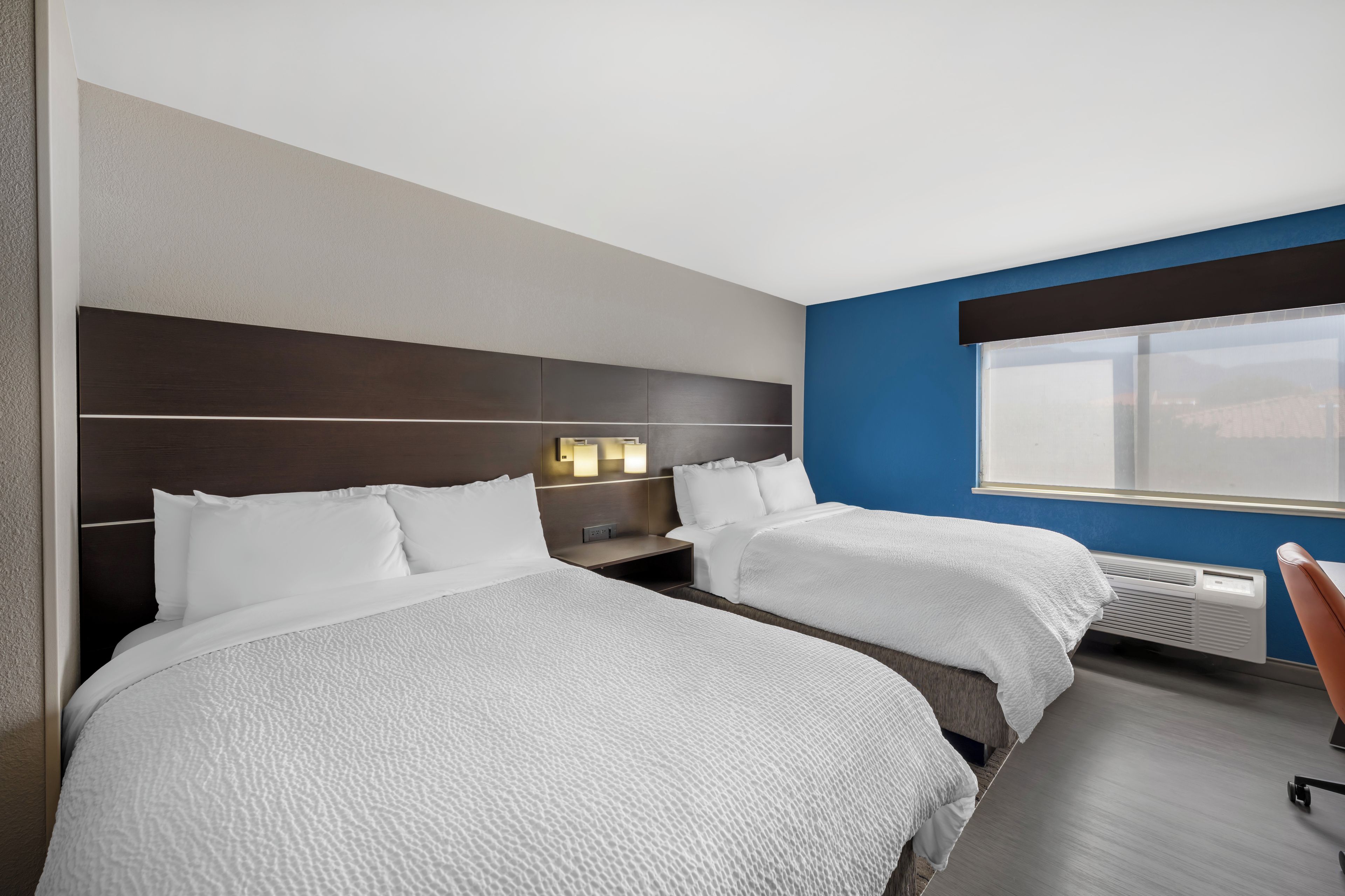 A hotel room with two beds, a desk, and a window.