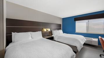 A hotel room with two beds, a desk, and a window.