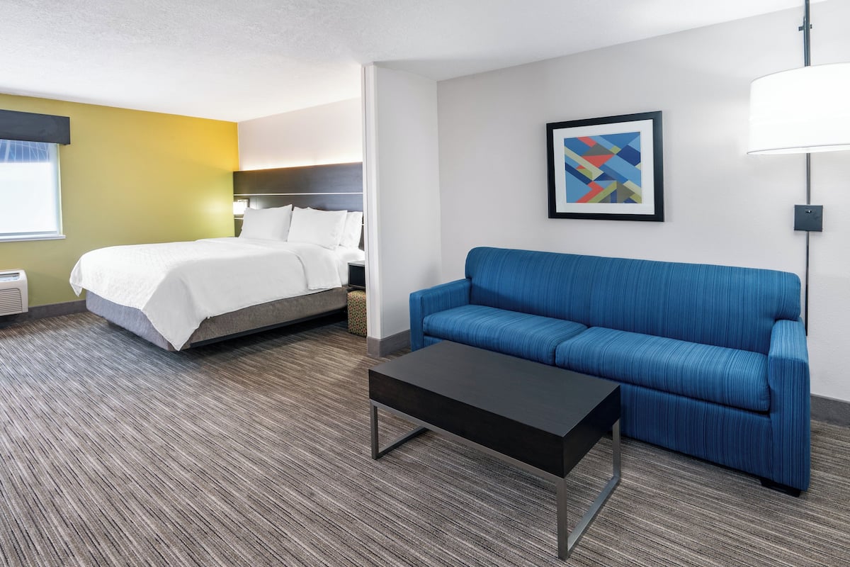 Une chambre d’hôtel avec un lit, un canapé bleu, une table basse noire et une lampe fixée au mur.