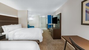 Une chambre d’hôtel avec deux lits, un bureau, une chaise, une télévision et une porte donnant sur une salle de bain.