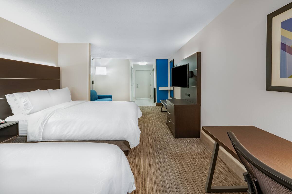 Une chambre d’hôtel avec deux lits, un bureau, une chaise, une télévision et une porte donnant sur une salle de bain.