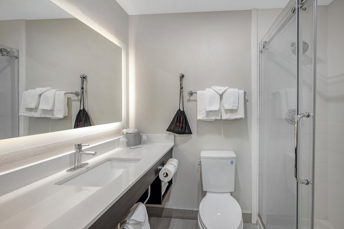 A modern bathroom with a large mirror, a white sink, a toilet, and a glass-enclosed shower.