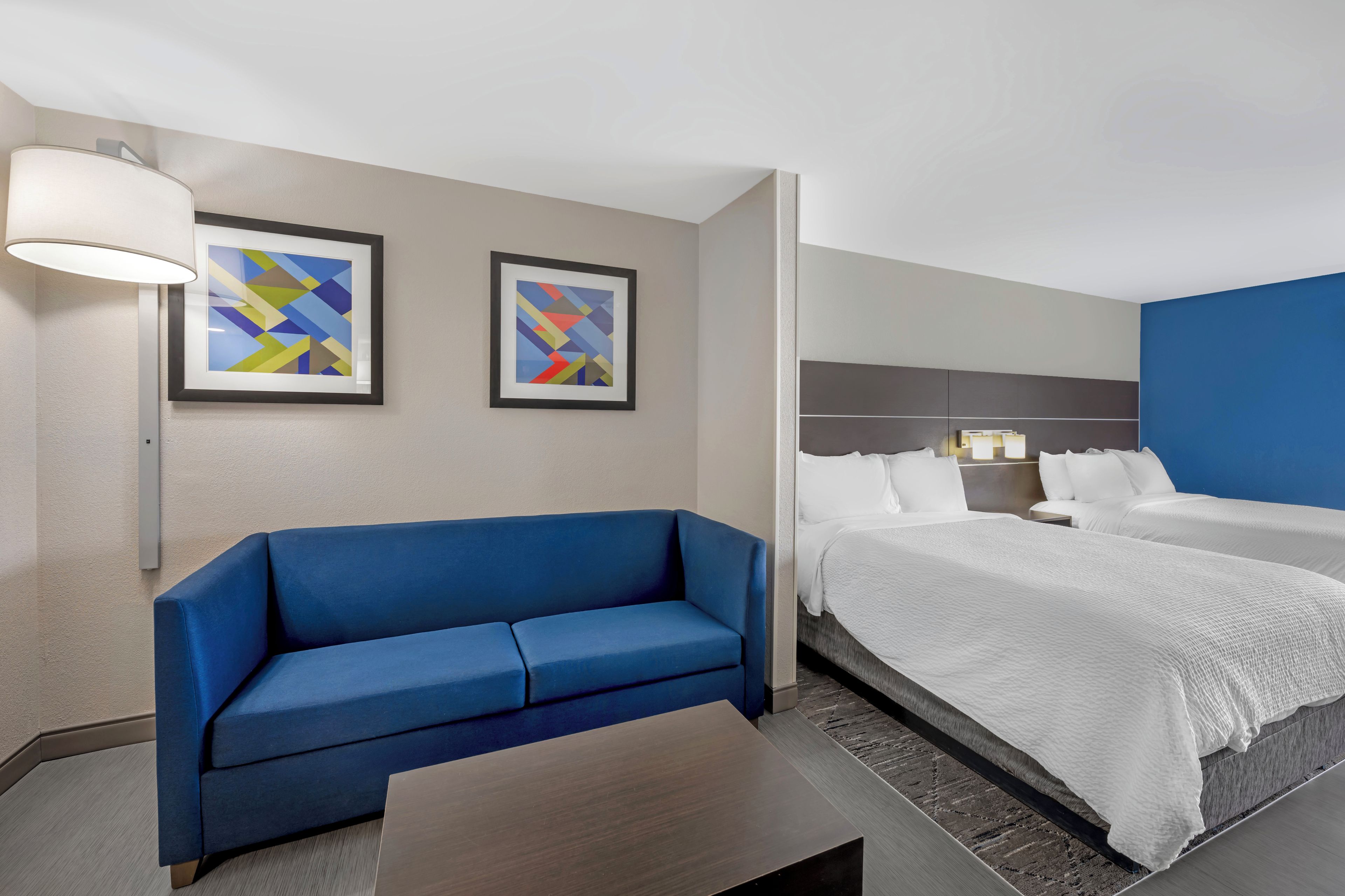 A hotel room with a blue sofa, a bed with white bedding, and two abstract paintings on the wall.
