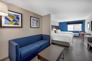 Een hotelkamer met een blauwe bank, een bed met wit bedlinnen, een bureau met stoel en twee abstracte schilderijen aan de muur.