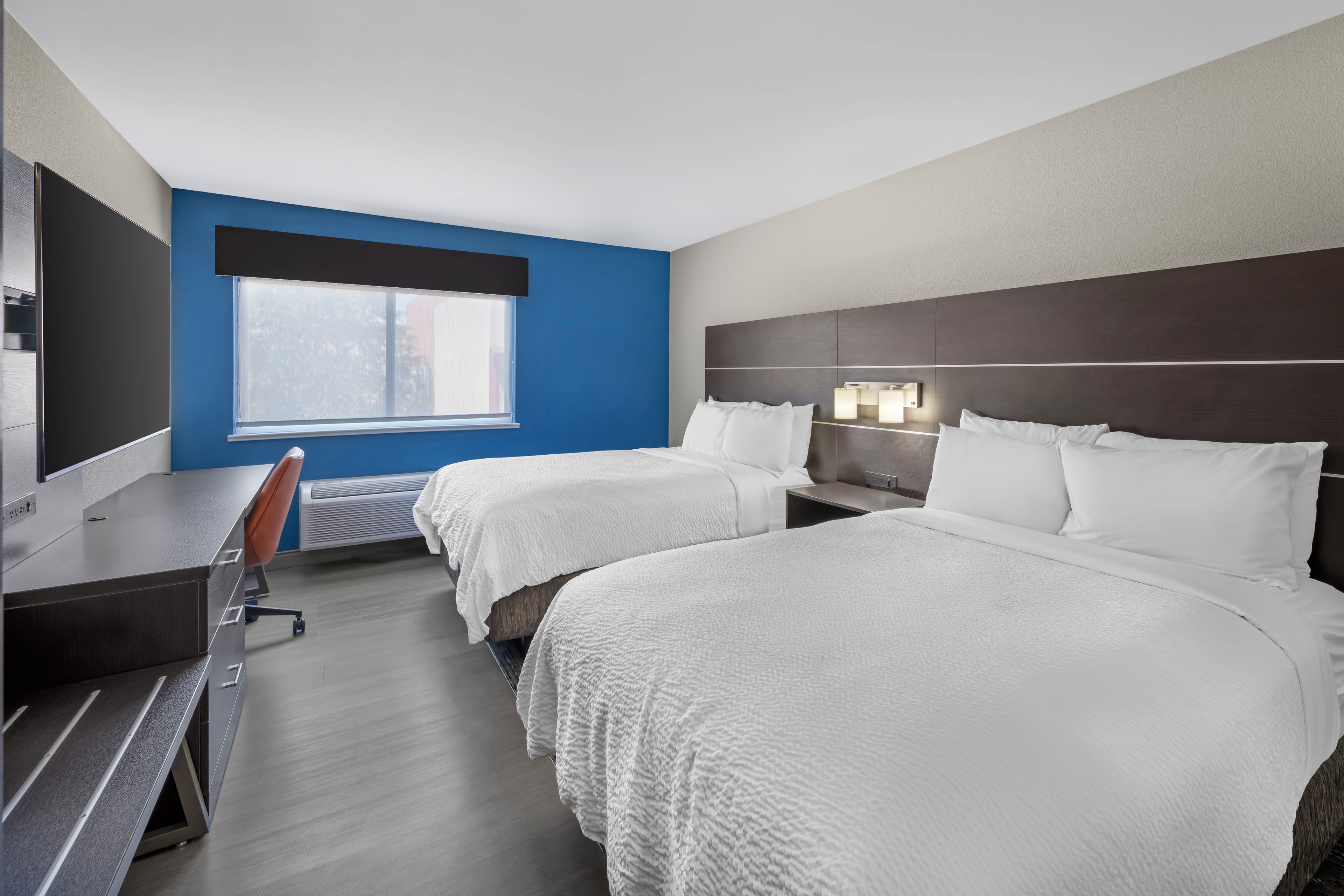 A hotel room with two beds, a desk, and a window.