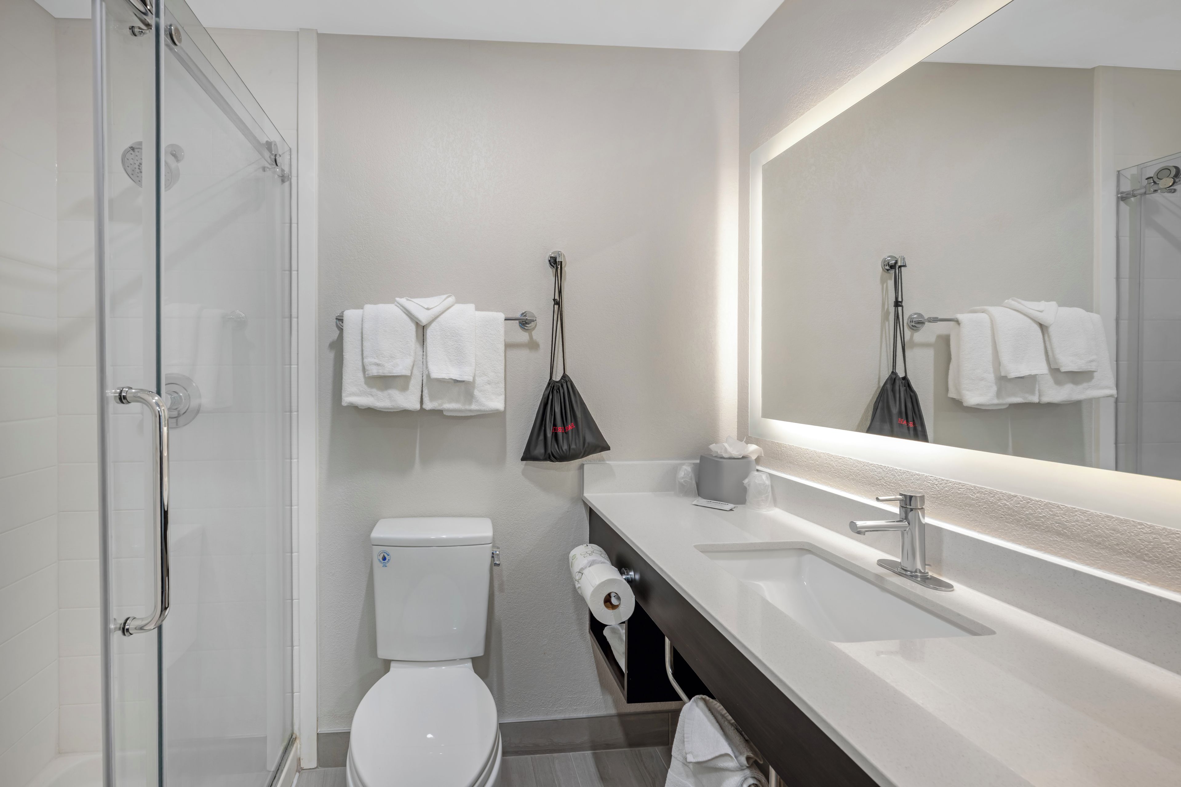 A modern bathroom with a glass shower enclosure, a white toilet, a sink with a mirror, and a towel rack with white towels.