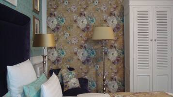 Quarto com cama, duas luminárias de cabeceira, um guarda-roupa e papel de parede floral.