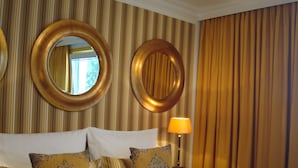 A hotel room with a large bed, multiple pillows, two wall-mounted mirrors, a bedside table with a lamp, and a curtain. - Hotel Sir & Lady Astor (Düsseldorf)