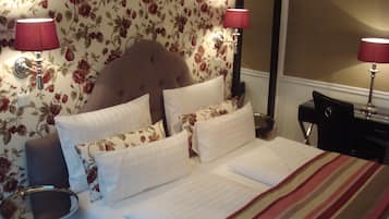 Una cama bien tendida con ropa de cama blanca y a rayas, un papel tapiz floral y dos lámparas de noche.