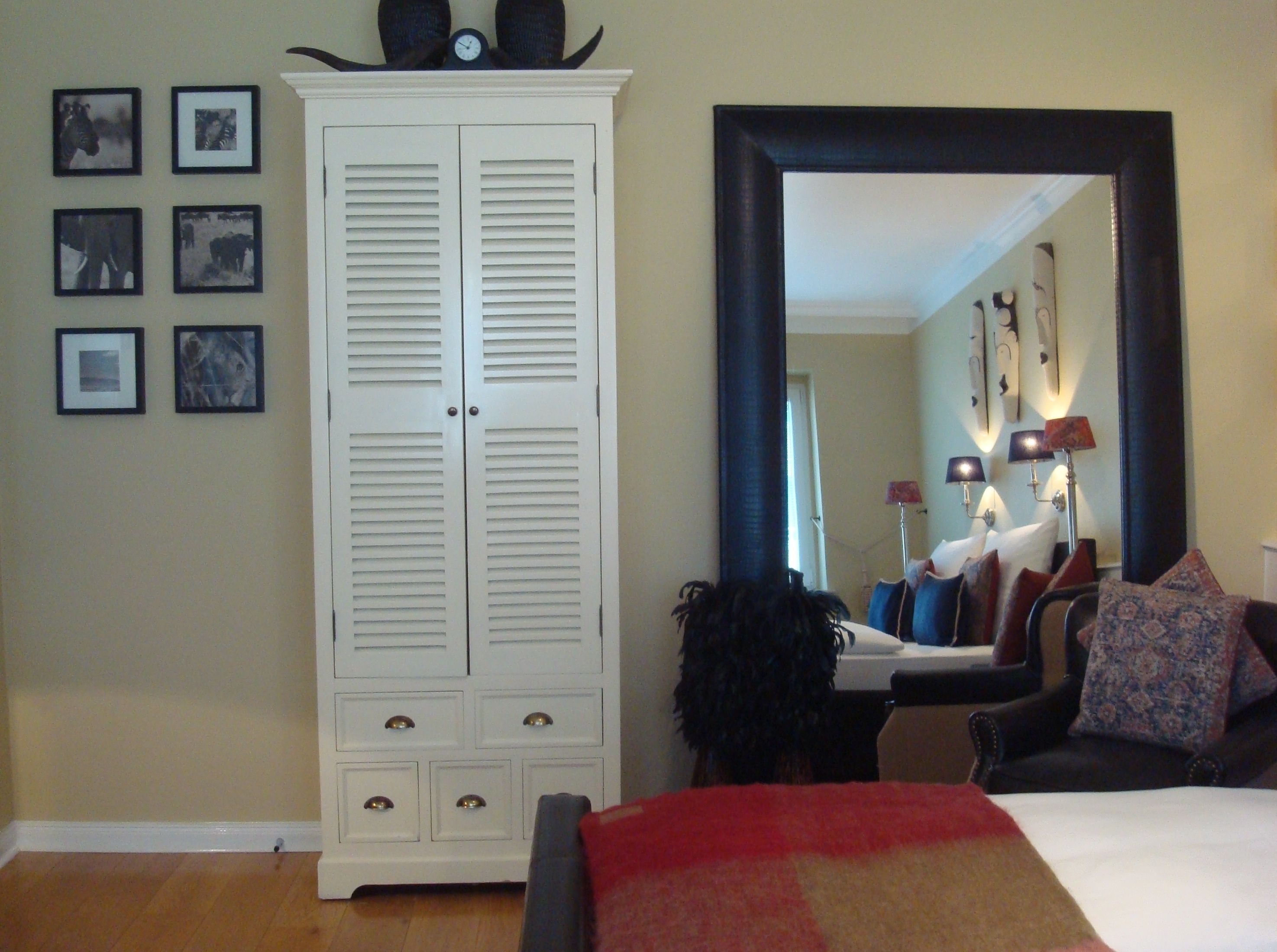 A bedroom with a large wardrobe, a bed with a red and beige blanket, a black armchair, and a large mirror on the wall.