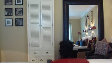 A bedroom with a large wardrobe, a bed with a red and beige blanket, a black armchair, and a large mirror on the wall.