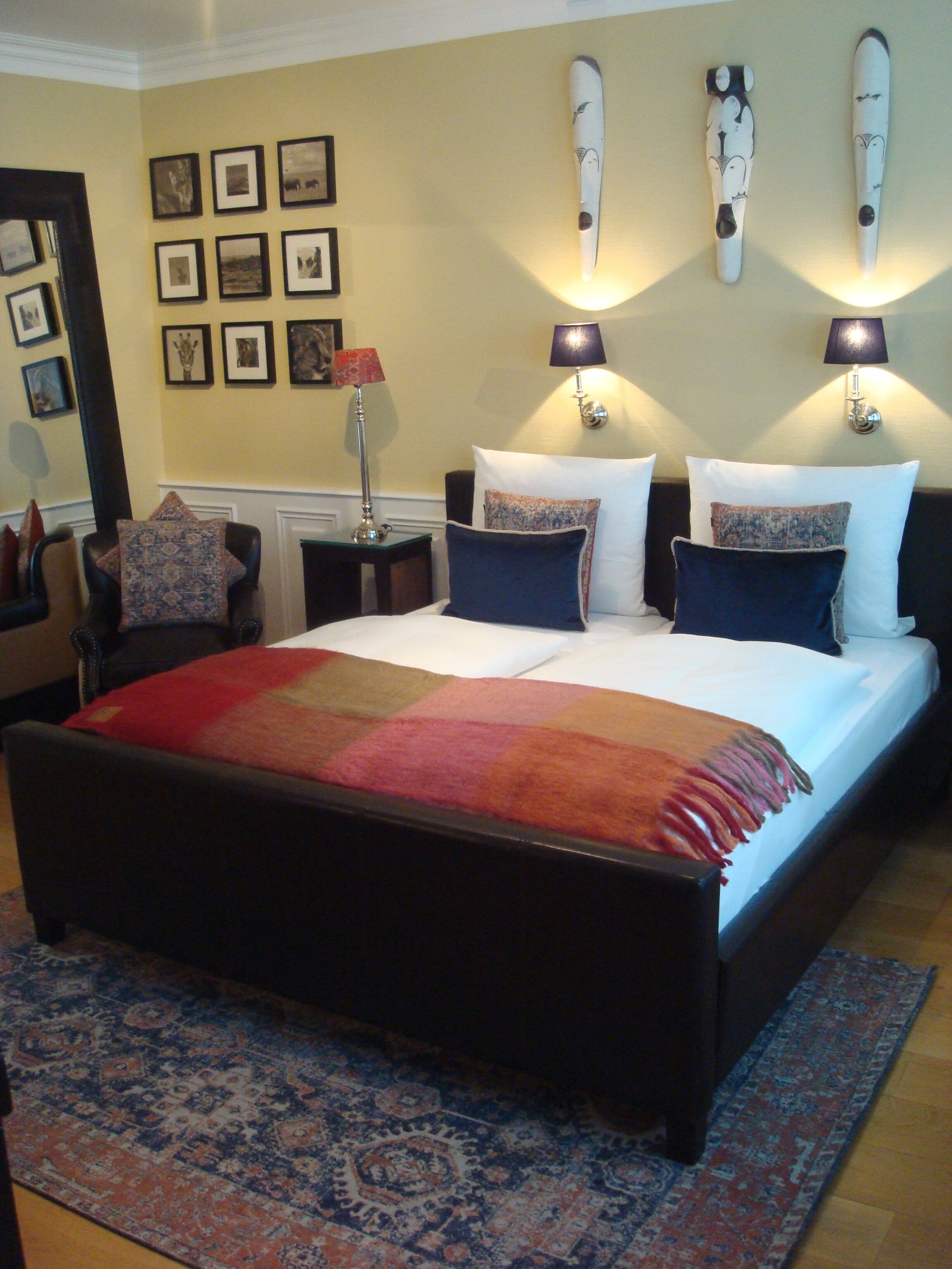 Un dormitorio ordenado con una cama grande, dos lámparas de noche y una pared decorada con cuadros.