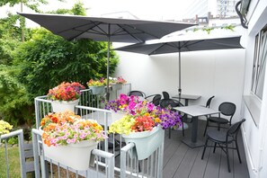 Un patio al aire libre con varias mesas y sillas, rodeado de macetas con flores de colores.