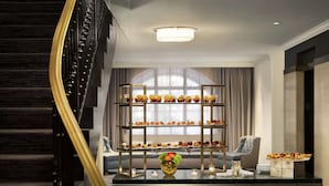 Un hall d’hôtel moderne avec un présentoir à trois niveaux rempli de desserts, un escalier et un coin salon offrant une vue sur la ville.