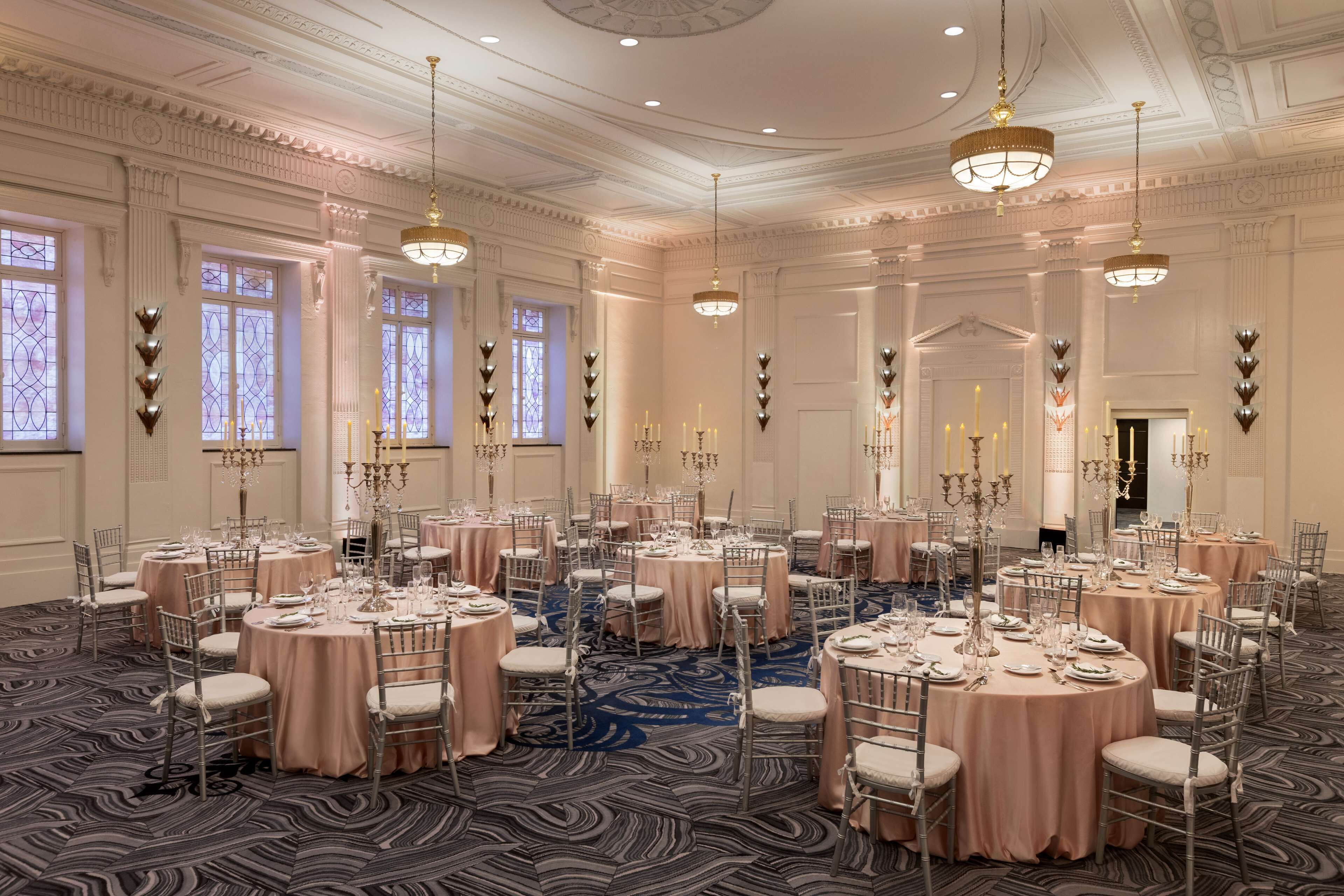 A banquet hall with round tables, chairs, chandeliers, and a patterned carpet.