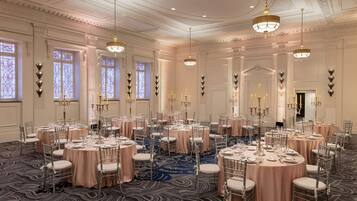 A banquet hall with round tables, chairs, chandeliers, and a patterned carpet.