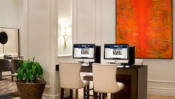 A modern interior with two monitors on a desk, a large abstract painting, and a potted plant.