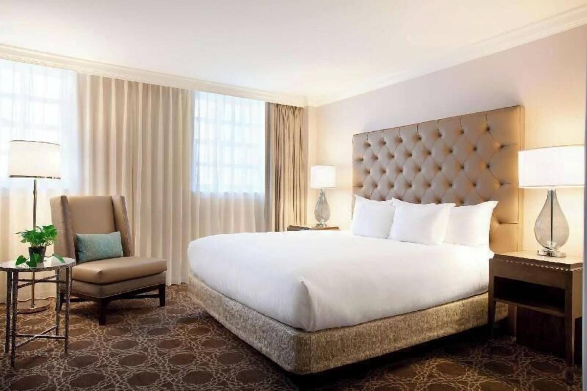 Una habitación de hotel con una cama grande, una silla, una mesita y una lámpara.