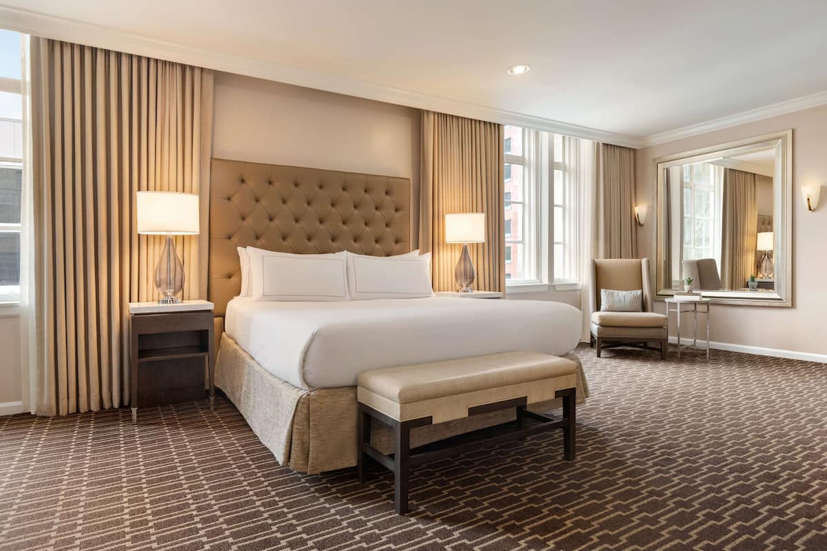Una habitación de hotel con una cama grande, un banco, una silla, un escritorio y un espejo.