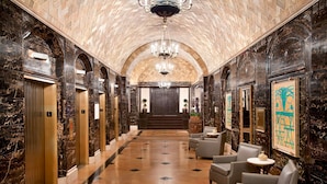Un hall d’entrée aux murs de marbre, doté d’ascenseurs, d’un lustre et d’un espace salon.