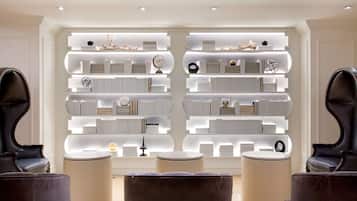 Un intérieur moderne avec une bibliothèque symétrique où sont exposés des livres et des objets décoratifs, deux fauteuils sombres et un pouf rond.