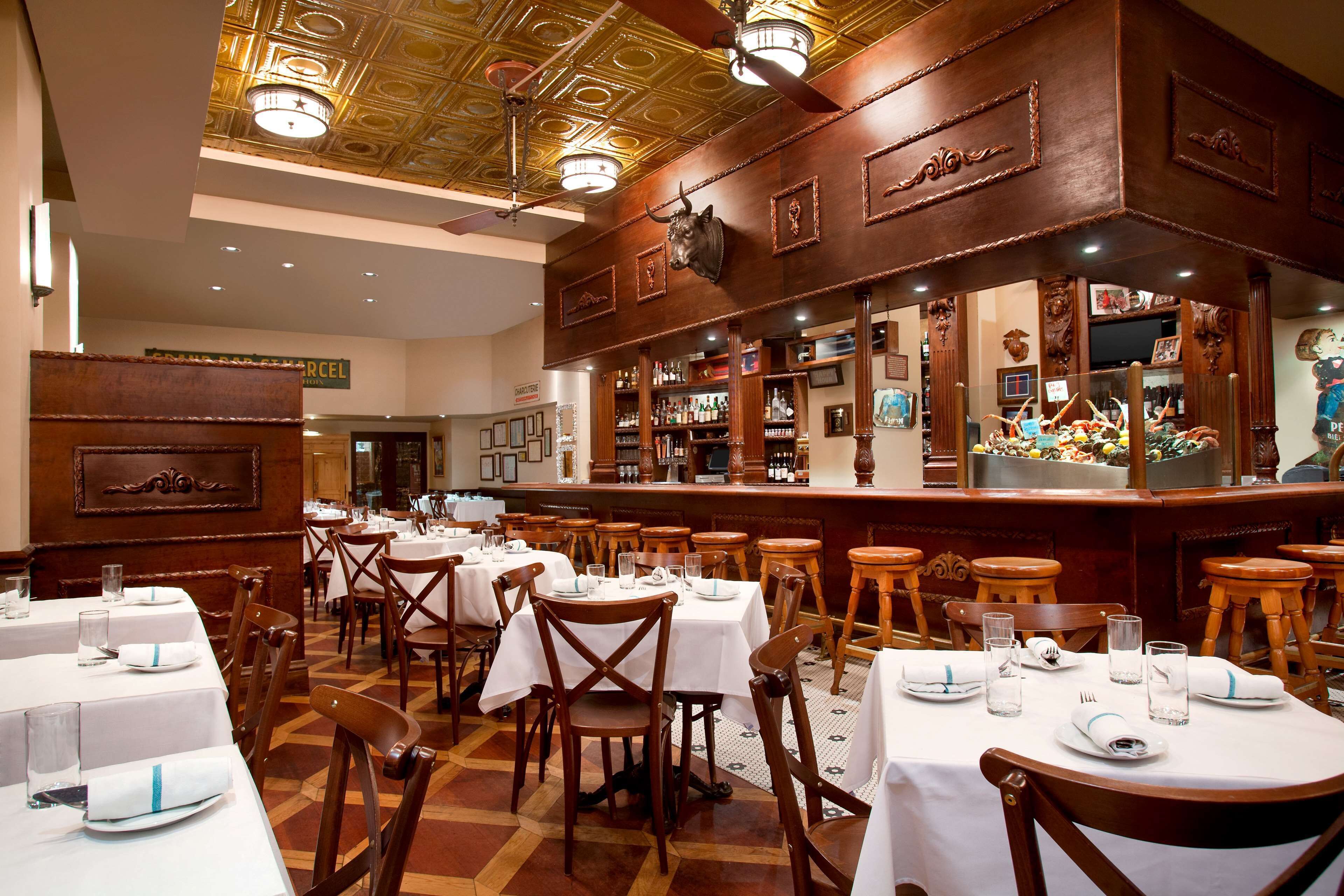 En restaurant med flere borde og stole, et barområde og et loft med dekorative detaljer.