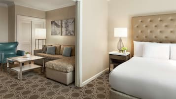 A hotel room with a large bed, a sofa, a chair, a small table, and a nightstand with a lamp.