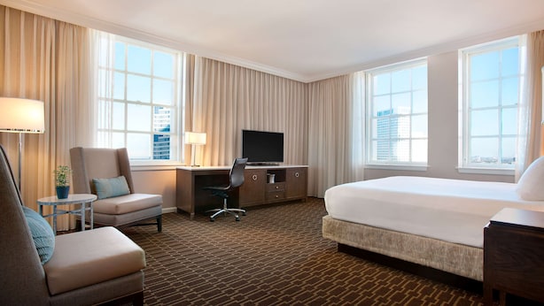 Une chambre d’hôtel avec un lit, un bureau avec une télévision, une chaise et une petite table avec une lampe.
