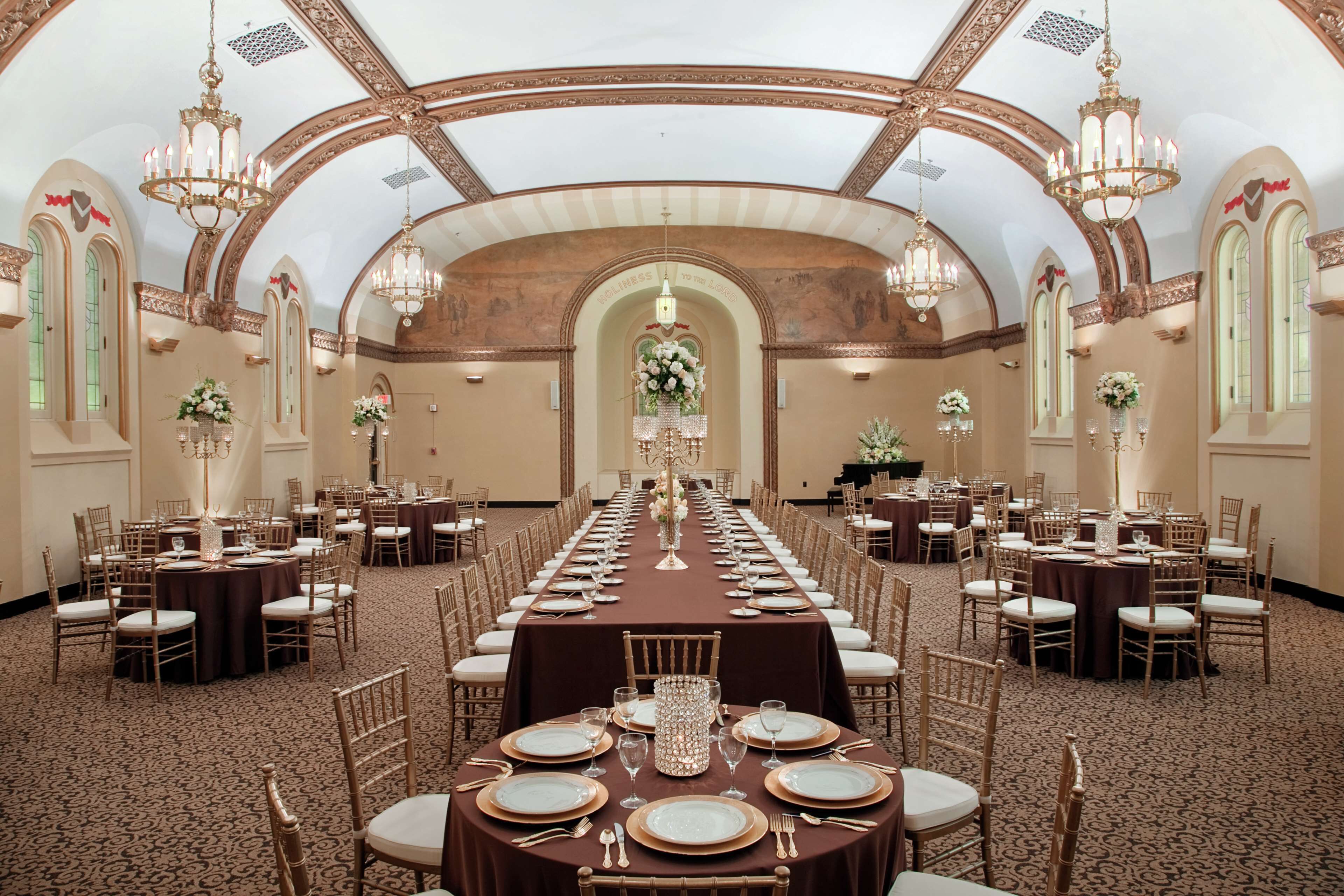 Un salón de banquetes con largas mesas dispuestas para cenar, candelabros y arreglos florales.