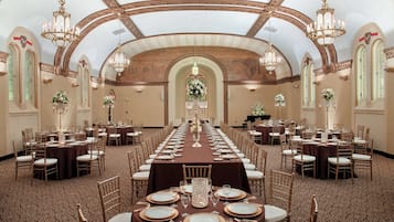 Un salón de banquetes con largas mesas dispuestas para cenar, candelabros y arreglos florales.