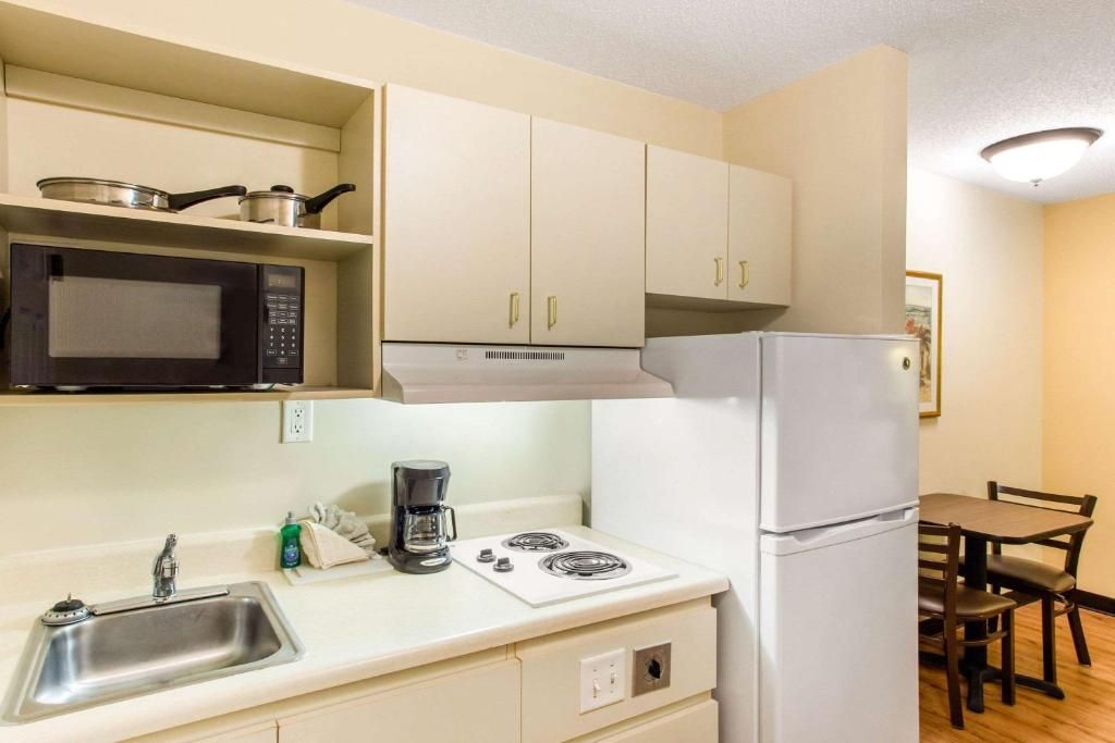 A compact kitchen with a microwave, stove, sink, and white cabinets.