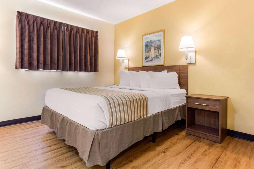Una habitación de hotel con una cama, lámparas de noche, una mesita de noche y un cuadro en la pared.