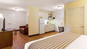 A compact hotel room with a bed, a desk, a sofa, a kitchenette, and a door. - Studio 6 Extended Stay - Myrtle Beach, SC (Myrtle Beach)
