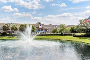 A hotel with a fountain in the foreground, a parking lot, and an American flag. - Studio 6 Extended Stay - Myrtle Beach, SC (Myrtle Beach)