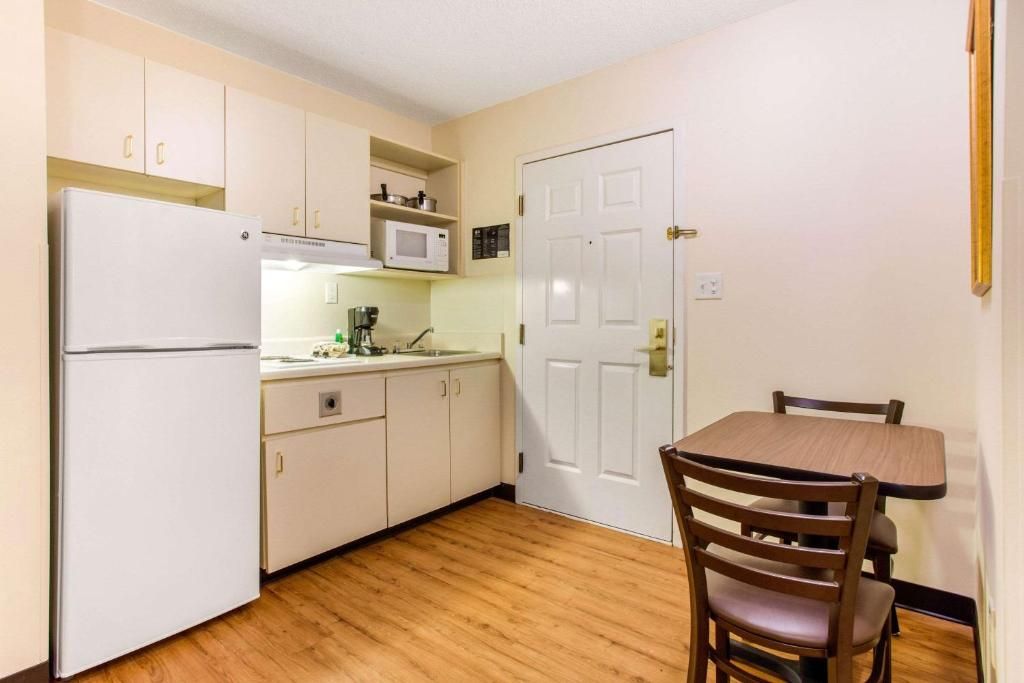 A compact kitchen with a refrigerator, microwave, and cabinets, a dining table with chairs, and a white door.
