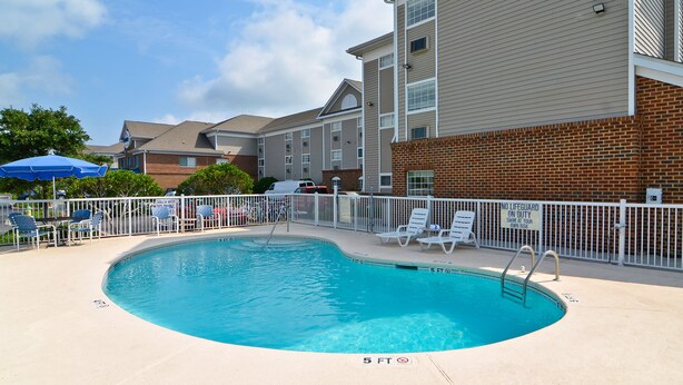A swimming pool with a 5 ft depth, surrounded by a white fence, and adjacent to a building with brick and siding exteriors. - Studio 6 Extended Stay - Myrtle Beach, SC (Myrtle Beach)