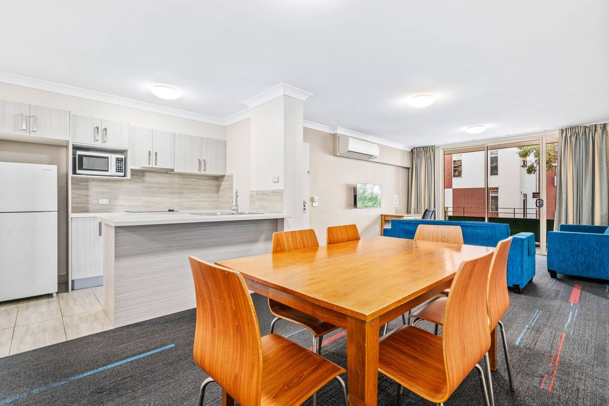 A modern kitchen with white cabinets, a microwave, and a dining area with a wooden table and chairs.