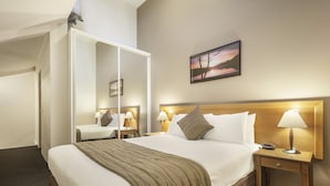 A hotel room with a large bed, a wooden headboard, two bedside tables with lamps, a mirror, and a painting on the wall. - APX Parramatta (Rosehill)