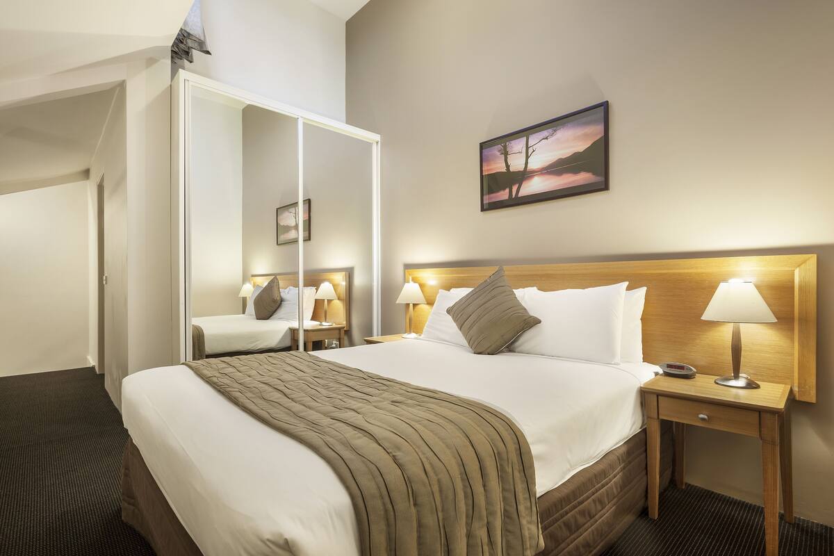 A hotel room with a large bed, a wooden headboard, two bedside tables with lamps, a mirror, and a painting on the wall.