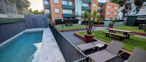 A courtyard with a swimming pool, lounge chairs, and a barbecue area.