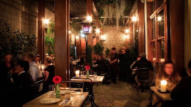 An indoor dining area with brick walls, wooden beams, and hanging lights. Tables are set with plates, glasses, and cutlery. - APX Parramatta (Rosehill)